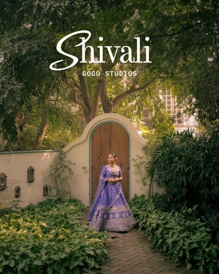Bride in a purple lehenga standing near a window during her wedding day in Gurugram, captured by Gogo Studios.